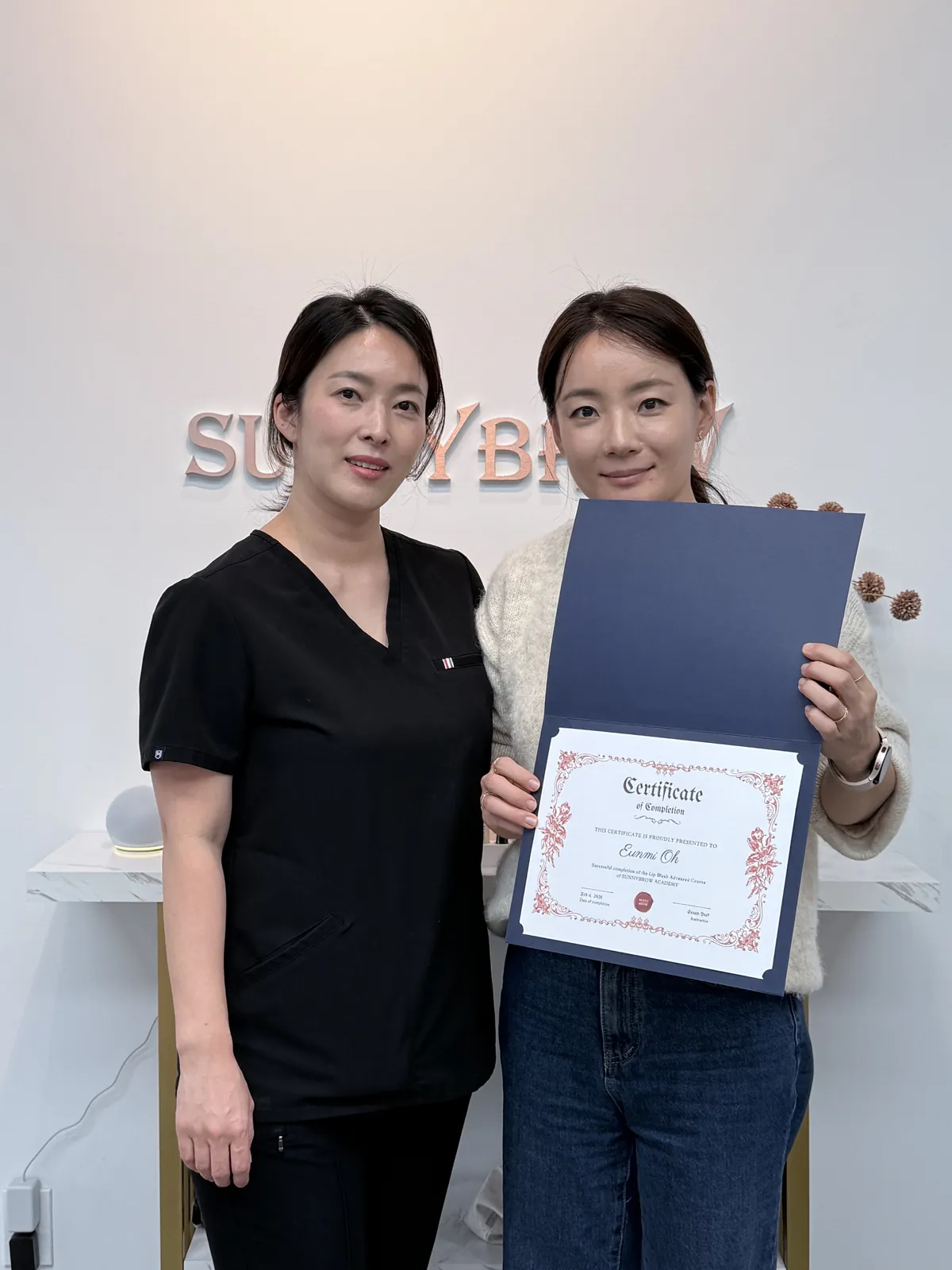 반영구 교육 과정을 마친 써니브로우 아카데미 수료생이 Sunny 원장과 함께 수료증을 들고 있는 모습