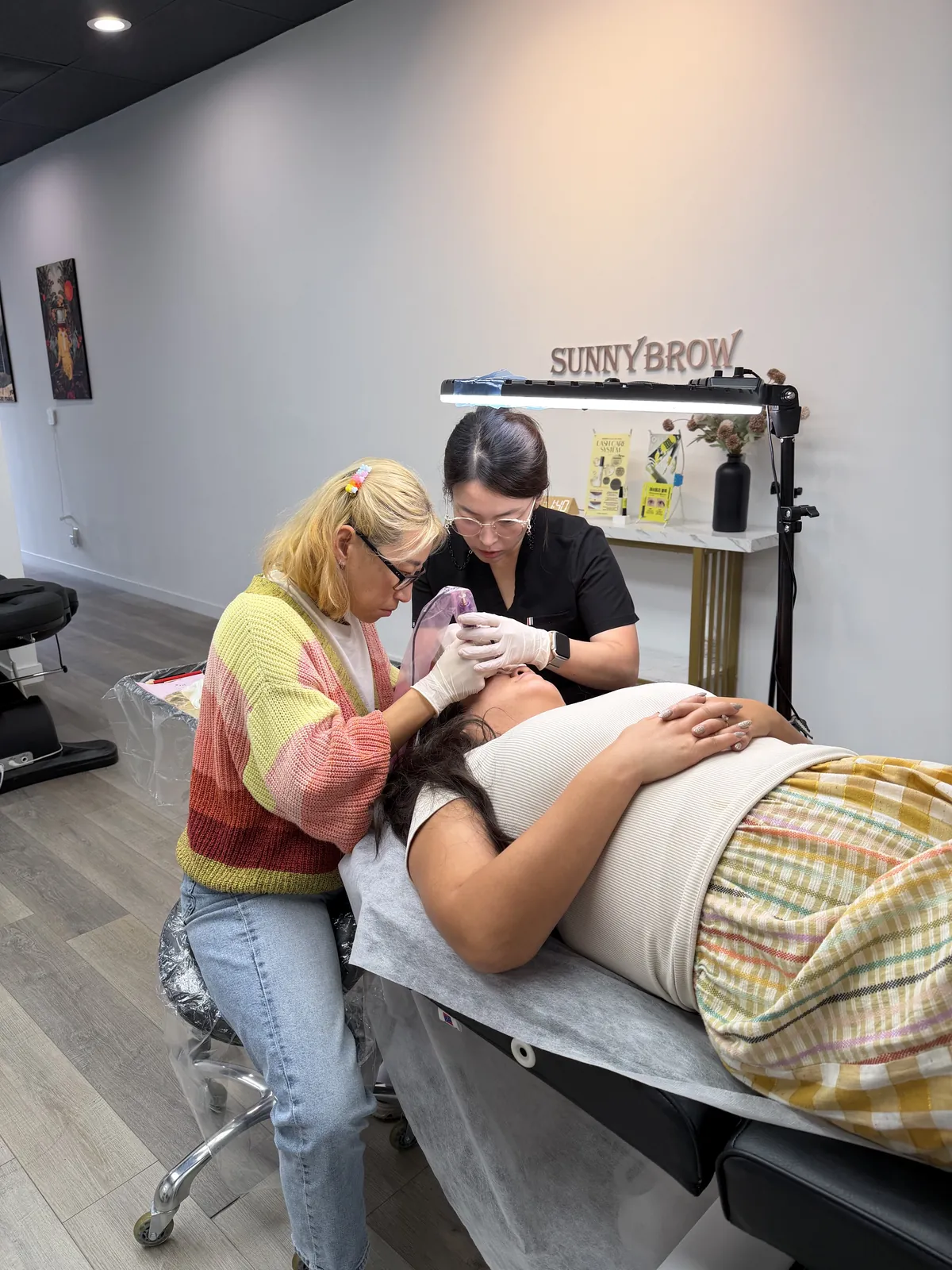 Student performing eyebrow permanent makeup on a live model under instructor supervision at SUNNYBROW Academy in Los Angeles